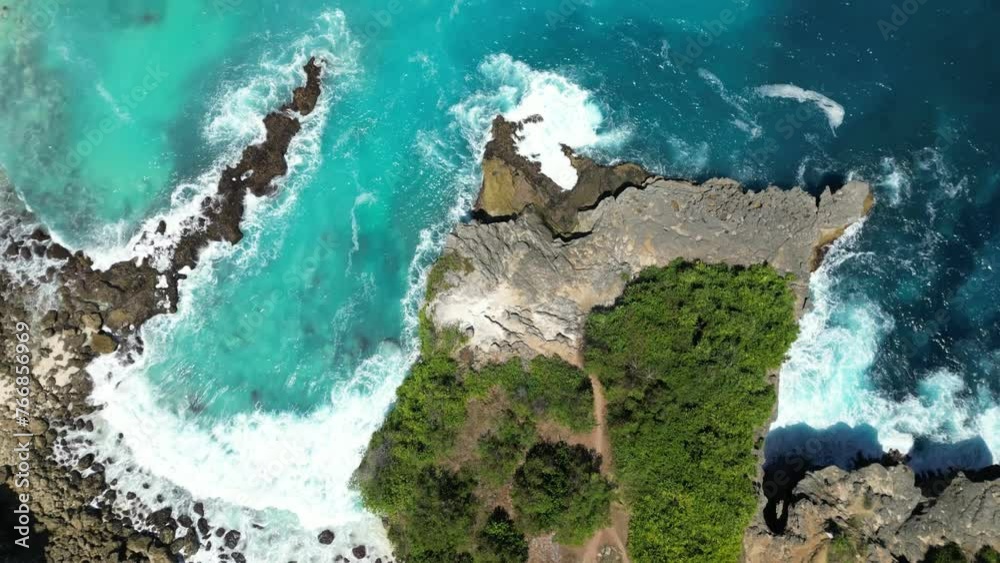 Aerial shot of ocean waves, stone cliff and ocean landscape in Bali, Indonesia in 4K. The drone flies over green cliff, turquoise blue water on a sunny day. Lembongan Island, Bali, Indonesia