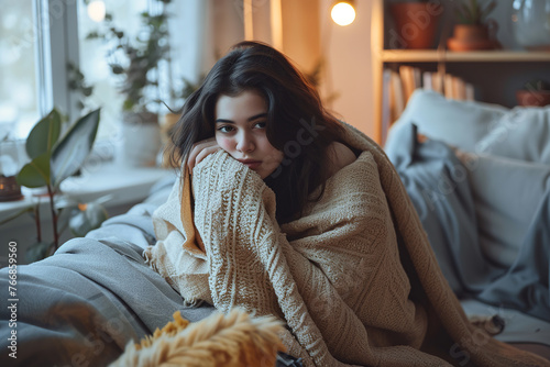 Young woman sits on sofa and sadly look. Winter cold and flu concept. Sick girl having influenza symptoms coughing at home, flu concept. photo