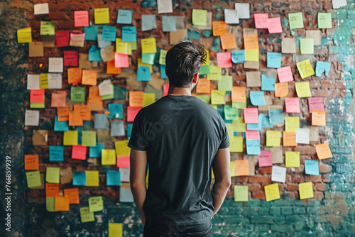 A picture of man standing in front of a wall covered in sticky notes, Man stand at wall with stick many colorful notes