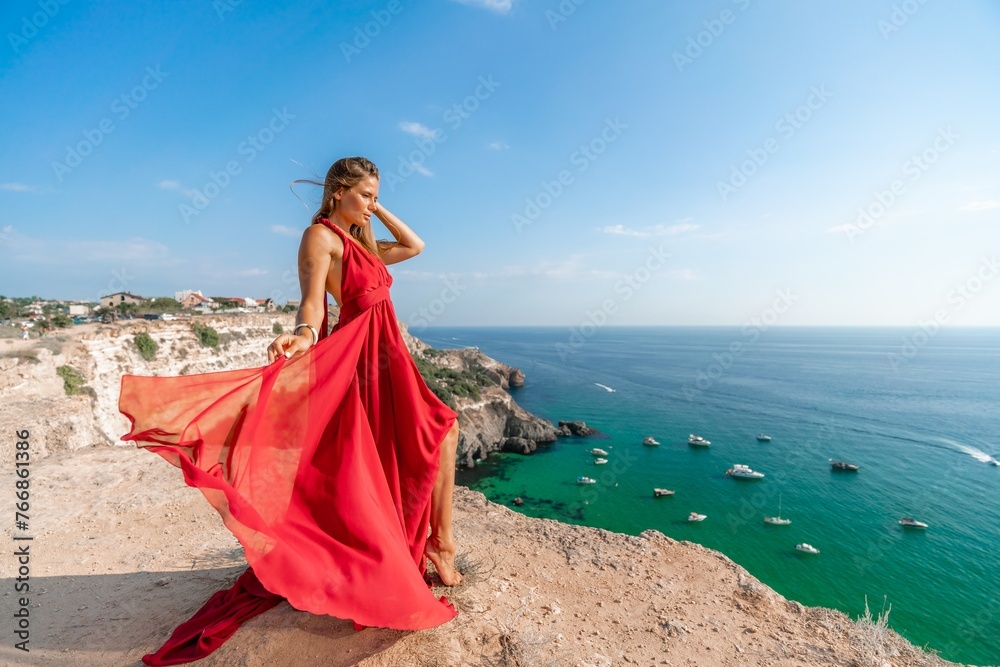Woman sea red dress yachts. A beautiful woman in a red dress poses on a cliff overlooking the sea on a sunny day. Boats and yachts dot the background. Woman sea red dress yachts. A beautiful woman in a red dress poses on a cliff overlooking the sea on a sunny day. Boats and yachts dot the background.