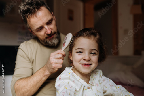 Foto Father combing and braiding daughter's hair as part of bedtime routine
