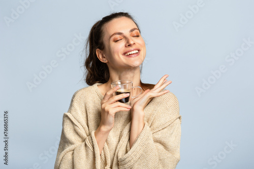 Portrait of a beautiful young lady enjoying a cup of black coffee. Isolated, light grey background.