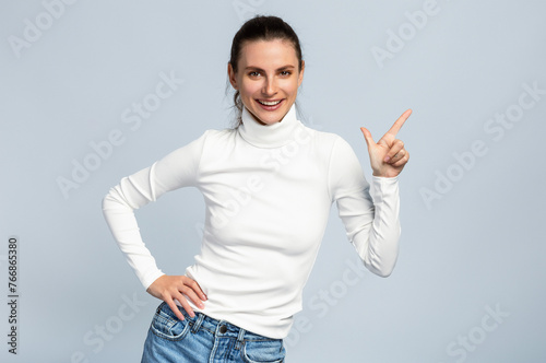 Portrait of an attractive woman pointing at blank space, white top, business style, on light grey studio background