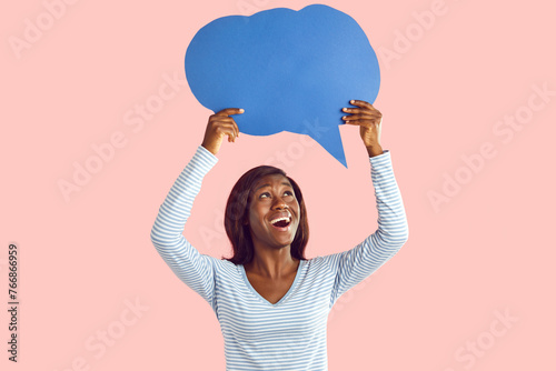 Happy excited young african american woman holding blank speech bubble for thoughts isolated on pink studio background. Girl with empty word cloud offering space for text. Idea concept.