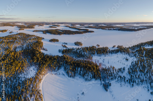 Aerial view over snow covered taiga landscape with boreal forest and frozen lakes in south Lapland, Finland at sunset