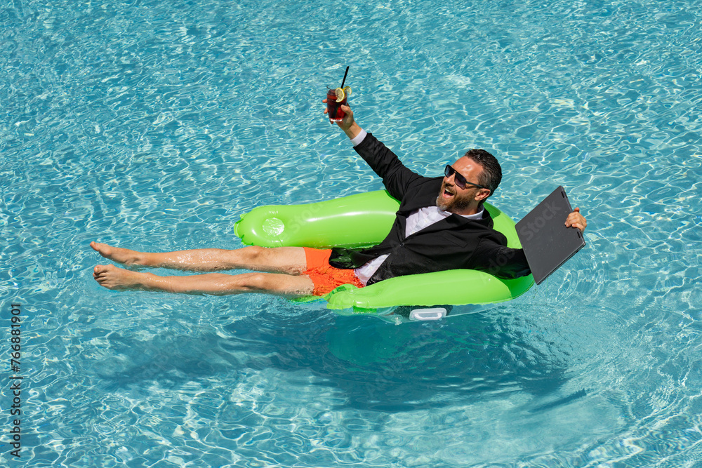 Funny business man in a business suit works for a laptop standing in the water in pool. Remote work. Crazy freelancer. Business and summer. Business man working online with computer laptop in pool.