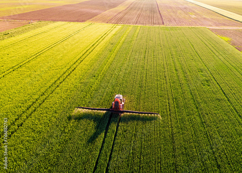 Drone shot of a red tractor fertilizing a lush green wheat field under the golden light of dusk