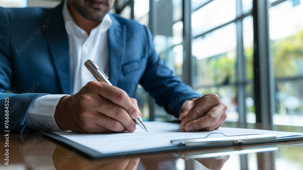 A man in a dark suit is sitting at a desk and writing on a notepad with a pen A man in a dark suit is sitting at a desk and writing on a notepad with a pen