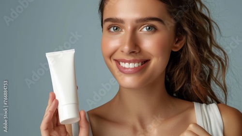 A woman holds a tube of cream in front of her face, showcasing the product