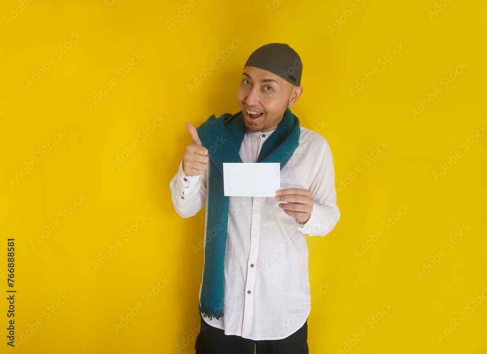 Happy Asian muslim man wear cap and scarf showing thumb up while holding envelope for mockup. Islamic zakat concept Happy Asian muslim man wear cap and scarf showing thumb up while holding envelope for mockup. Islamic zakat concept