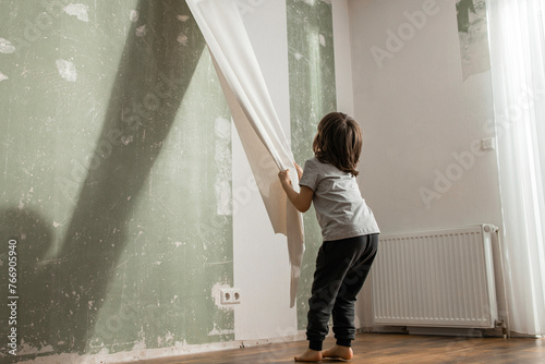 Boy peeling old wallpaper from wall in living room photo