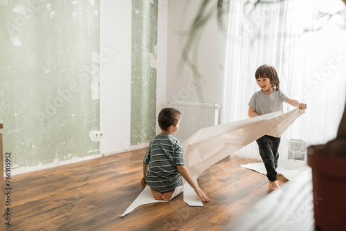 Boy pulling brother sitting on wallpaper and having fun at home photo