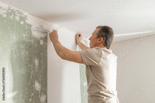 Man gluing white wallpaper in living room at home