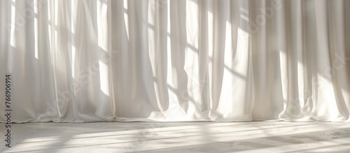 Light and shadows create lines on the curtain and cast silhouettes on the white wall on a sunny day with the sun s rays  providing a mockup with space for text.
