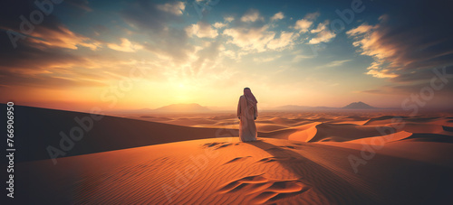 Panoramic image of the desert dusk, rear view of a traveller arabic man walking in the desert among the sand dunes at sunset.