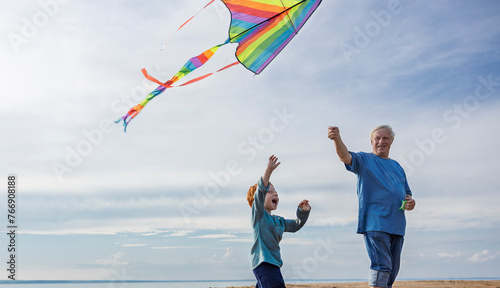 Elderly man flying kite with grandson at beach photo