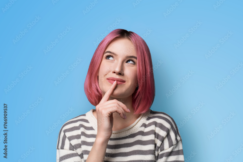 Portrait ad image - mysteriously grinning smile look up thinking gladly pink hair woman wear grey striped sweater jumper, hold finger over her she lips, isolated blue studio wall background. Portrait ad image - mysteriously grinning smile look up thinking gladly pink hair woman wear grey striped sweater jumper, hold finger over her she lips, isolated blue studio wall background.