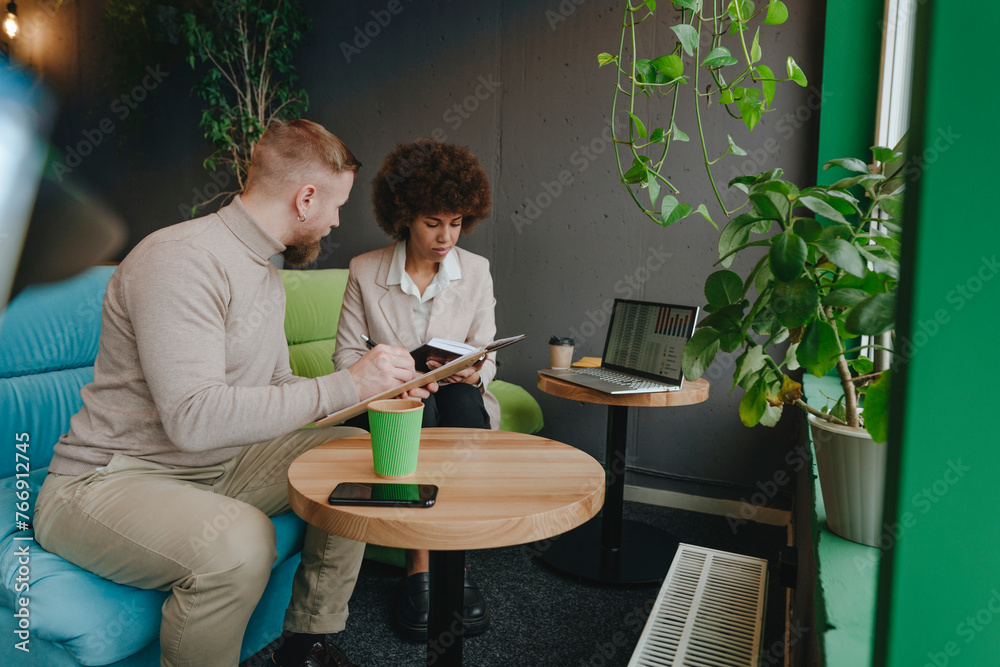 Business colleagues discussing over clipboard in coworking office Business colleagues discussing over clipboard in coworking office