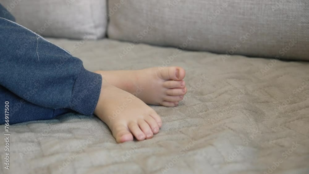 A small child sleeps on the sofa in the living room. The bare feet of a napping boy close-up on a soft blanket. The baby is resting after leisure games. He moves his legs and toes in his dreams A small child sleeps on the sofa in the living room. The bare feet of a napping boy close-up on a soft blanket. The baby is resting after leisure games. He moves his legs and toes in his dreams