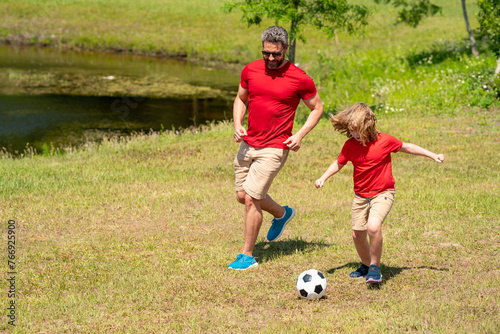 Father and son playing football in park. Dad and little boy play soccer. Sporty family enjoy summer day. Sport for kids. Football soccer game. Fathers day. Father and son kick ball on the green grass.