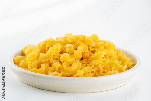 Dry, raw pasta Creste Di Gallo in a plate on a light background.