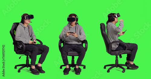 Adult uses vr gadgets for gameplay with smartphone app, sitting on gaming chair in isolated full body greenscreen. Asian male model playing multiplayer contest of virtual reality games. photo