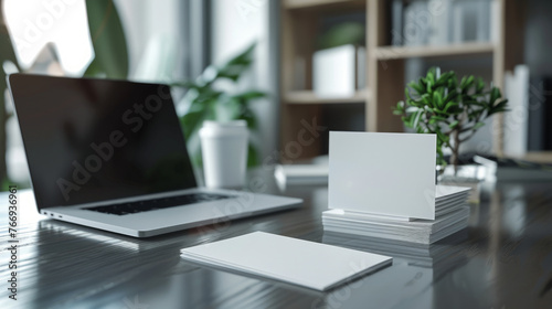 A modern workspace featuring a sleek laptop with a blank screen alongside stacks of blank business cards on a polished wooden desk. © ChubbyCat