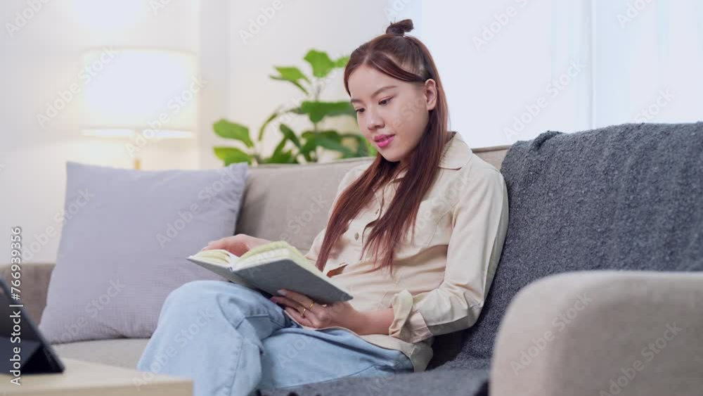 Asian businesswoman working from home, reading her work notebook on the sofa in the living room Asian businesswoman working from home, reading her work notebook on the sofa in the living room