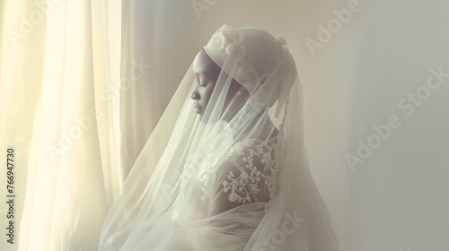 African bride wearing a white wedding dress facing a window in the morning light photo