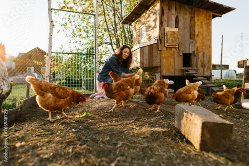 Happy middle aged woman on a private farm feeding chickens. Eco-friendly farmer woman cares, looks after her chickens in her backyard, promoting organic poultry farming photo