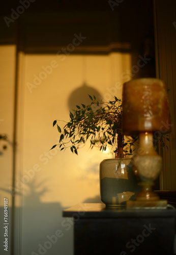 little table by a door, decorated with green plant and an antique lamp, seen in a golden sunset light