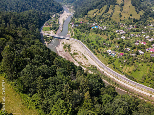 view of a road in the mountains, a river flows between the bridges, a village is located along the road between the mountains, a summer landscape