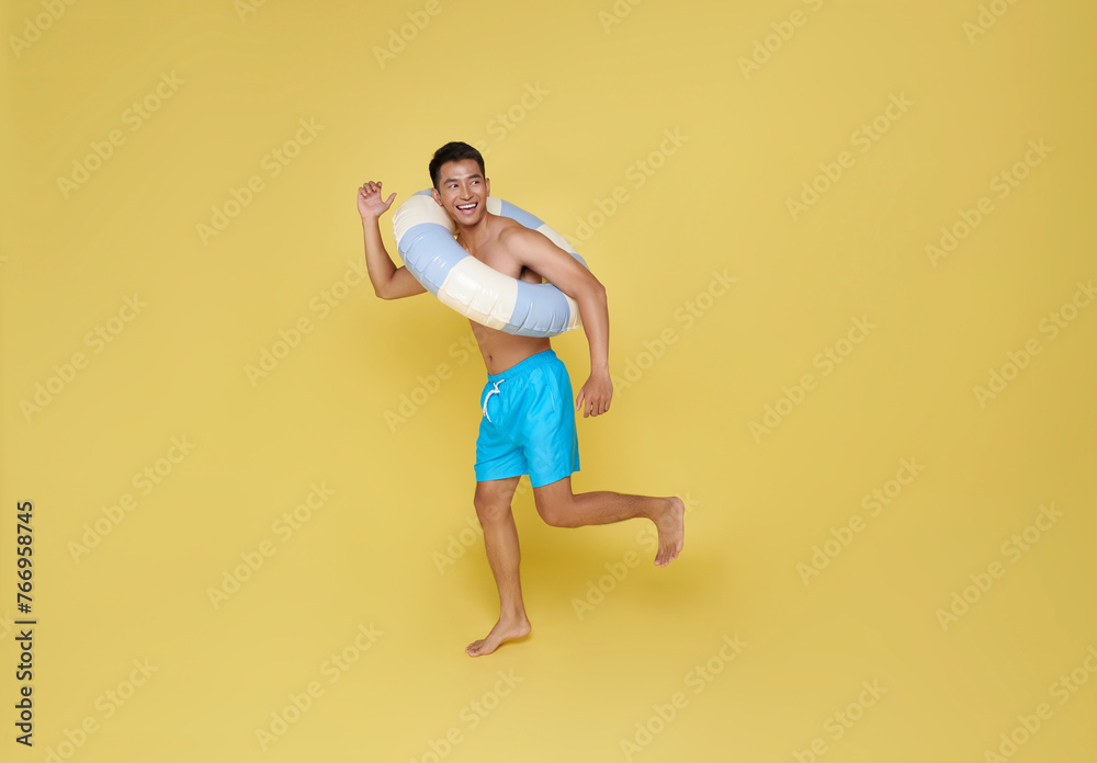 Full body young tourist asian man hold inflatable ring running happy summer vacation isolated on yellow background. Full body young tourist asian man hold inflatable ring running happy summer vacation isolated on yellow background.