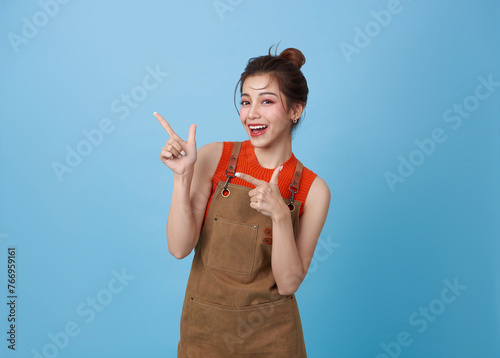 Portrait young asian barista woman wearing apron standing and pointing fingers isolated on blue background, waitress or entrepreneur cheerful, small business or startup,