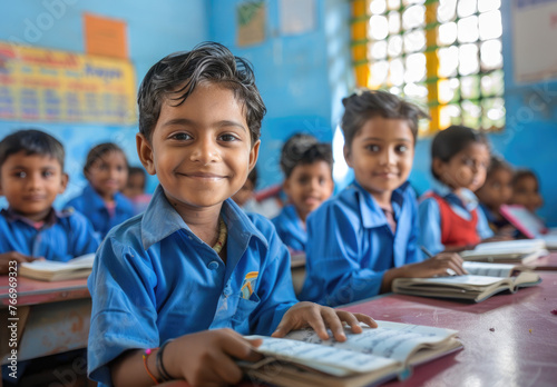 A school classroom full of happy India children  boys and girls wearing blue uniforms sitting at their desks reading books