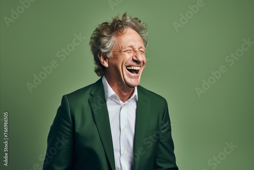 Portrait of a happy senior man laughing while standing against green background © Iigo