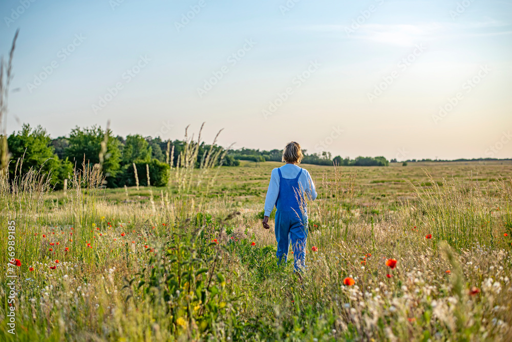 entspannte junge Frau läuft auf einer Blumenwiese, Rückansicht
