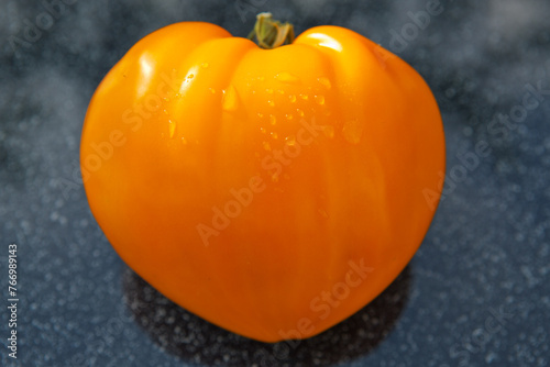 Big yellow tomato in shape of heart on gray background.