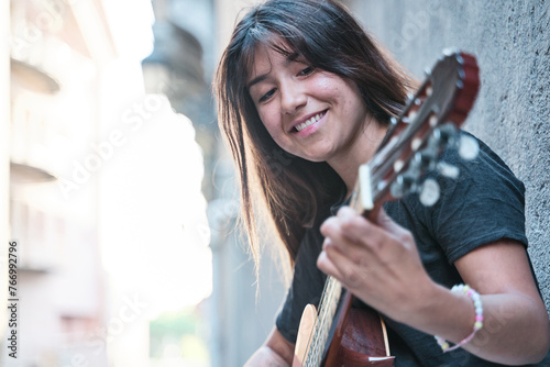 portrait of a brunette-haired latina woman playing the guitar. side view of a pretty woman smiling. photo