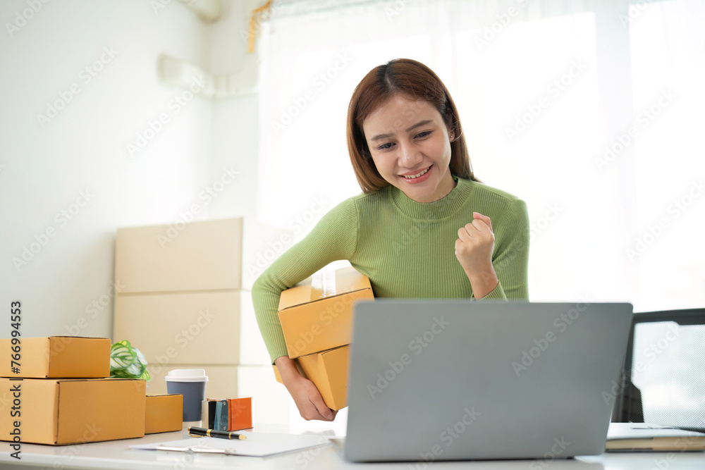 Startup SME small business entrepreneur of freelance Asian woman using a laptop with box Cheerful success Asian woman her hand lifts up online marketing packaging box and delivery SME idea concept Startup SME small business entrepreneur of freelance Asian woman using a laptop with box Cheerful success Asian woman her hand lifts up online marketing packaging box and delivery SME idea concept