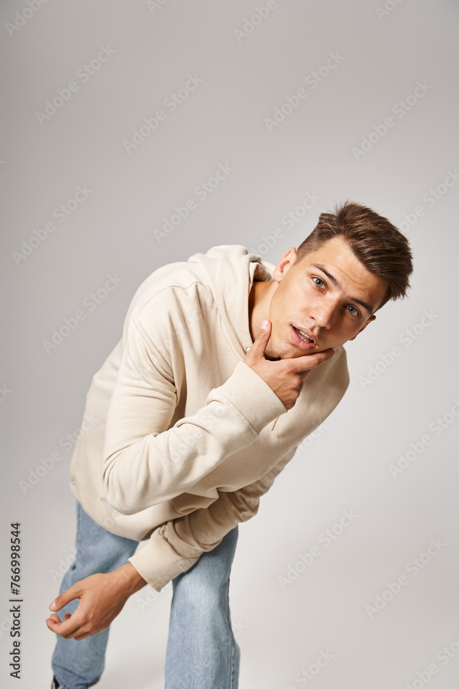charismatic young guy leaning to forward and touching to jawline against grey background charismatic young guy leaning to forward and touching to jawline against grey background