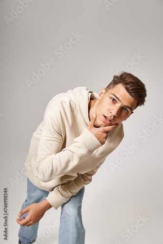 charismatic young guy leaning to forward and touching to jawline against grey background © LIGHTFIELD STUDIOS