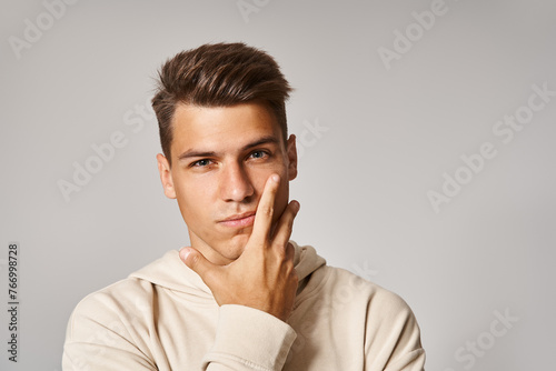 portrait of handsome young man with brown hair and grey eyes covering to cheek with hand