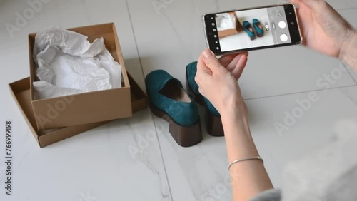 A young woman takes pictures of shoes with a smartphone to sell online. Second hands, second life of things. Online store for selling used items.
