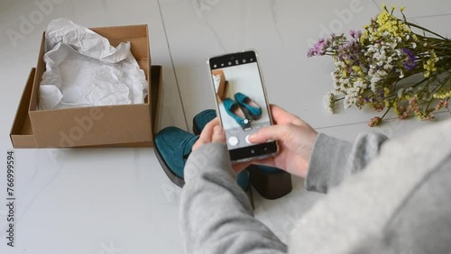 Young woman with a smartphone takes pictures of shoes to sell online. Second hands, second life of things. Online store for selling used items.