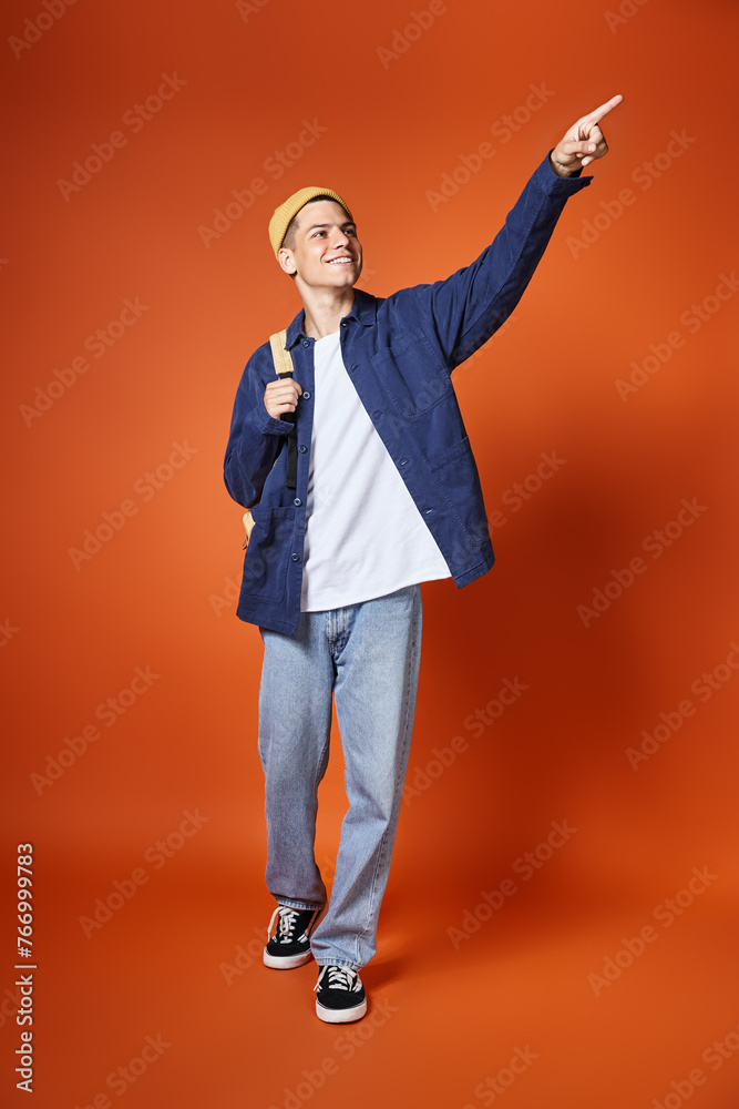 smiling student with backpack pointing with finger into distance on terracotta background smiling student with backpack pointing with finger into distance on terracotta background