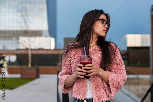 Modern woman enjoying a vegan smoothie with skyscrapper on background photo
