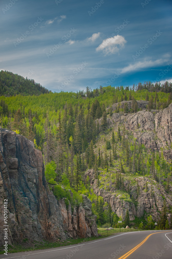 A scenic portrayal of a rough, rocky terrain covered with trees against a captivating sky with an interesting cloud formation