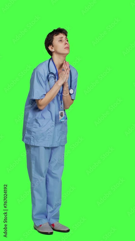 Side view Medical assistant being hopeful praying for good luck against greenscreen, holds hands in a prayer sign and having belief in spirituality. Young christian nurse with faith in meditation
