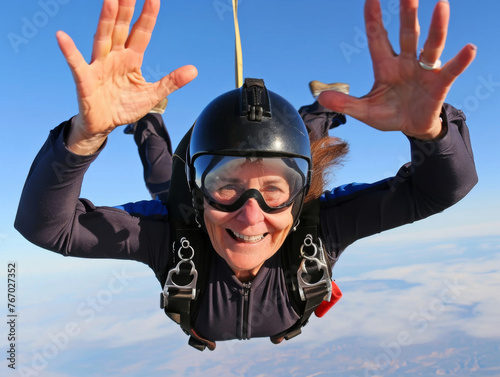 Mature woman jumping with a parachute, smiling, wearing glasses and helmet